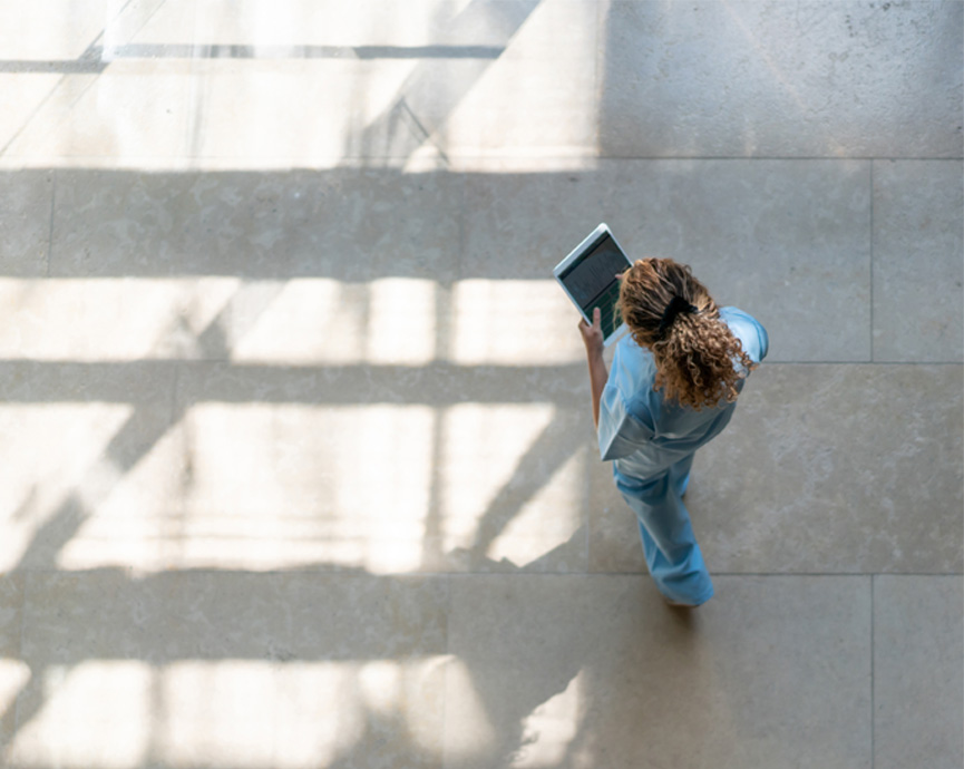 Person holding tablet walks across a paved surface.